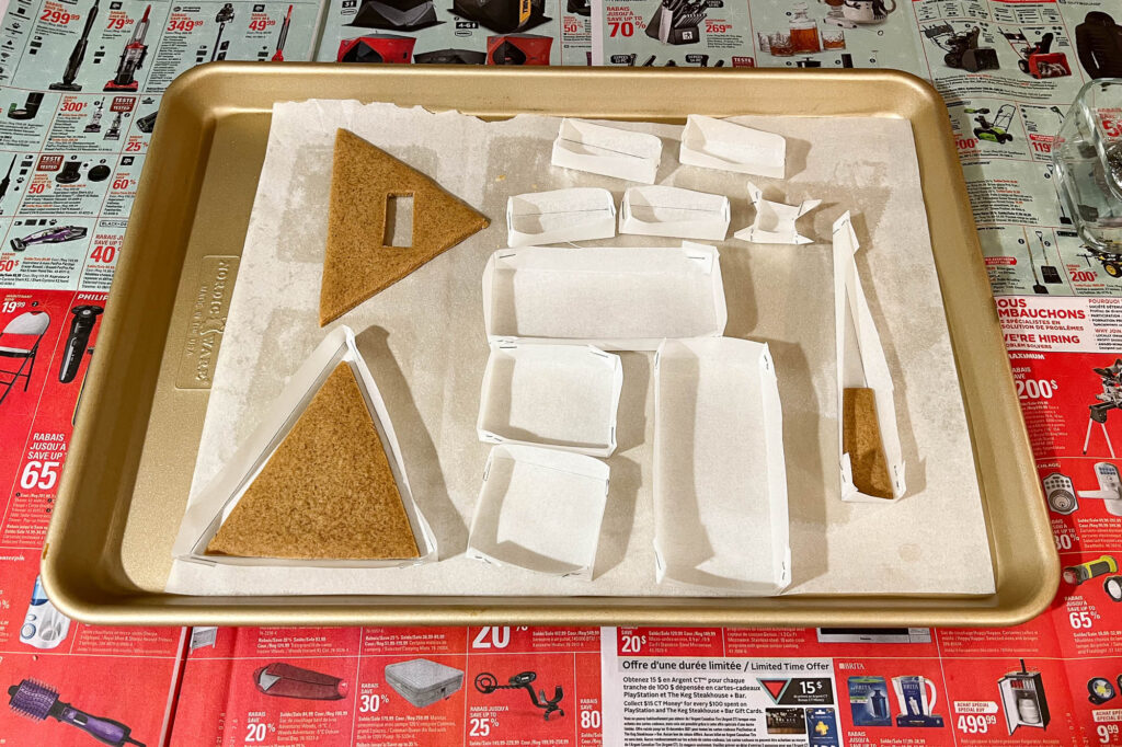 Baking tray with pieces of gingerbread and forms made out of baking paper.